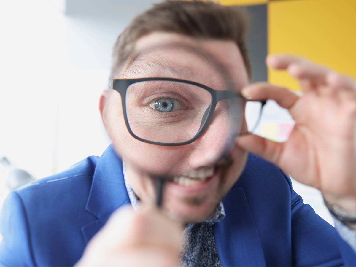 Człowiek w okularach z lupą. Obrazek w artykule Kiedy źrenice się powiększają? Poznaj przyczyny powiększania się źrenicy oka