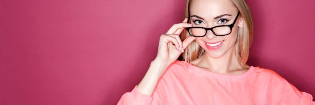 Kobieta w różowej bluzce w okularach. Obrazek w artykule Najmodniejsze oprawki do okularów. Poznaj już dziś nowe trendy okularów
